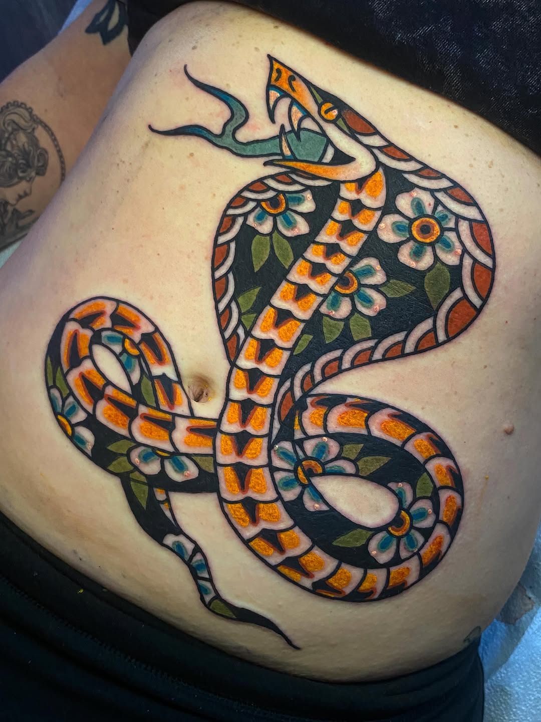 Ornate cobra snake with decorative floral patterning in orange, teal, and black on the thigh.