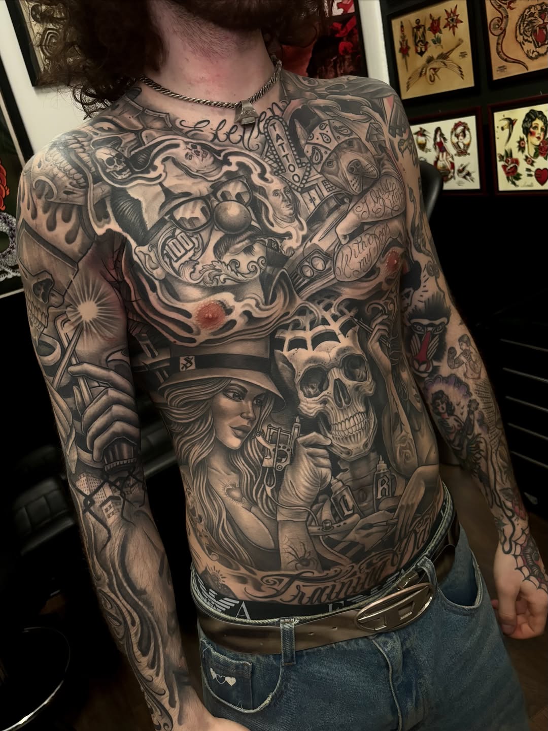 Full chest and sleeve tattoo featuring skulls, female portrait in top hat, ornate baroque designs, and various imagery in black and grey shading.