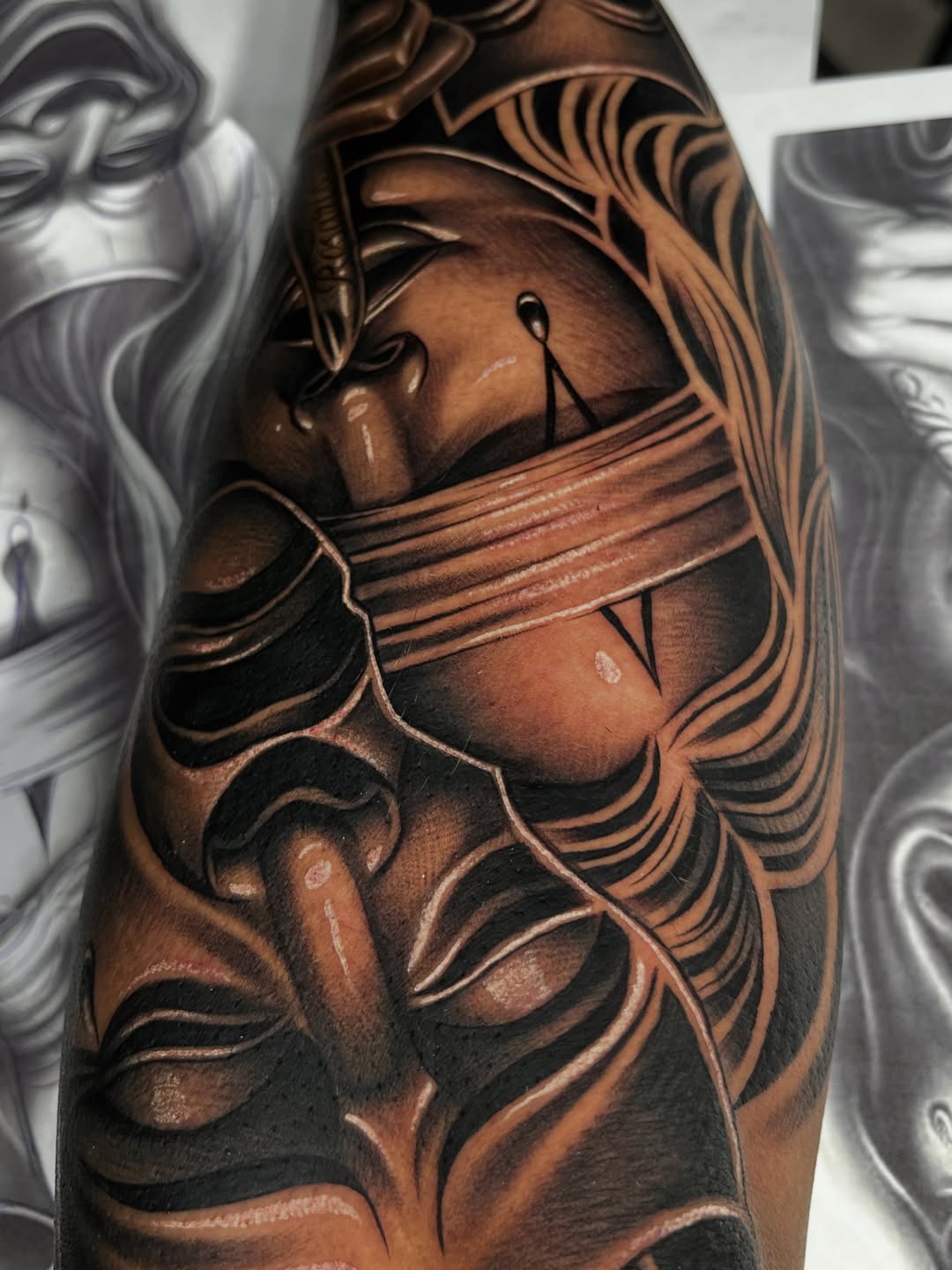 Black and grey tattoo on arm depicting a bandaged samurai or warrior mask with flowing wind lines and tears, done in realistic shading.