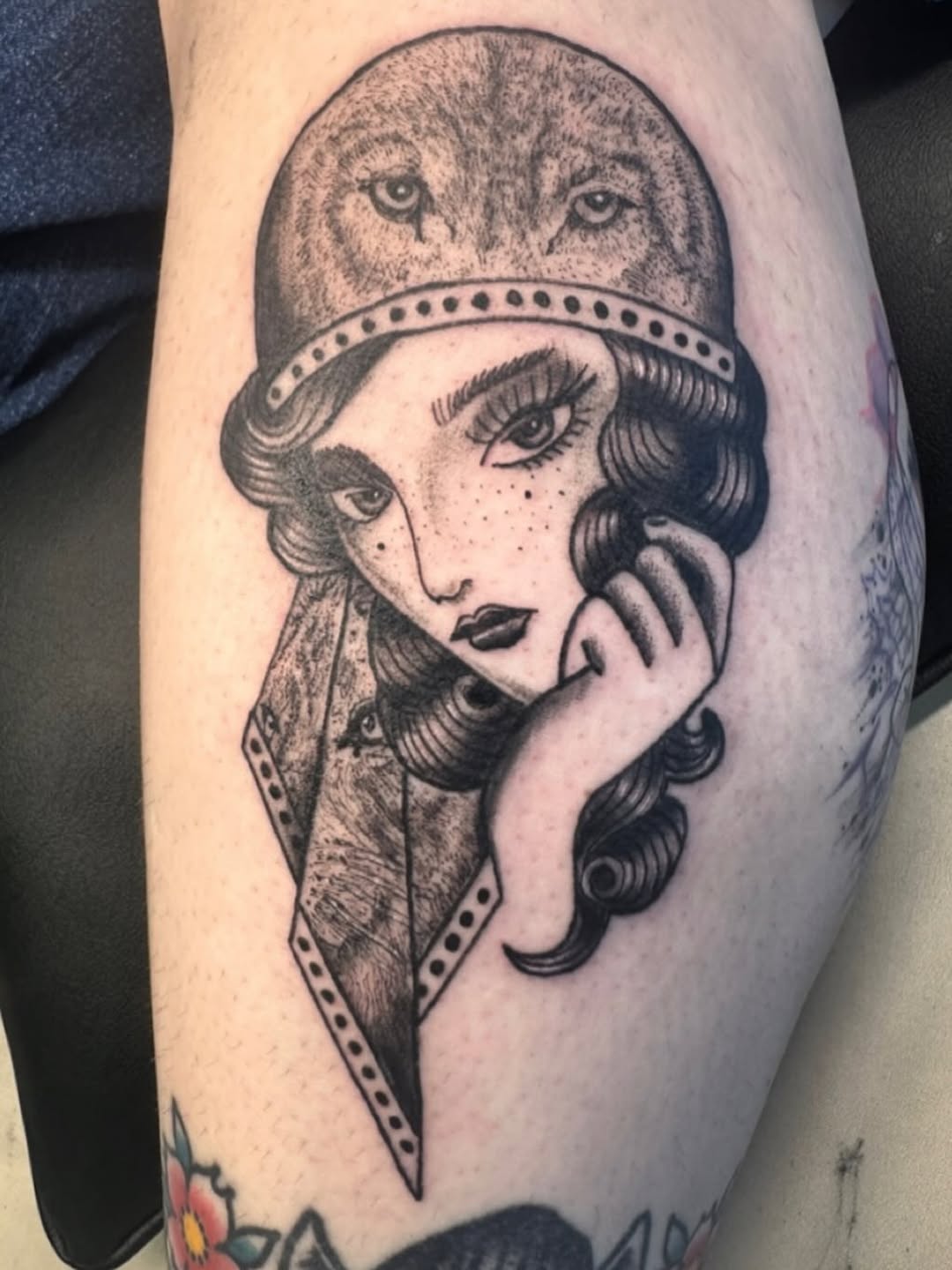 Black and grey portrait tattoo on upper arm of a woman wearing a headband with an owl perched above her head, detailed facial features and wavy hair.