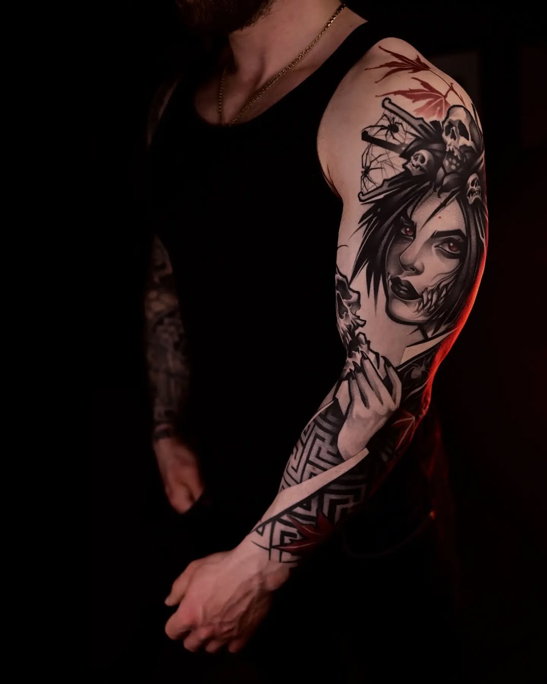 Full sleeve tattoo featuring portrait faces with skull imagery and geometric patterns in black and grey on male arm.