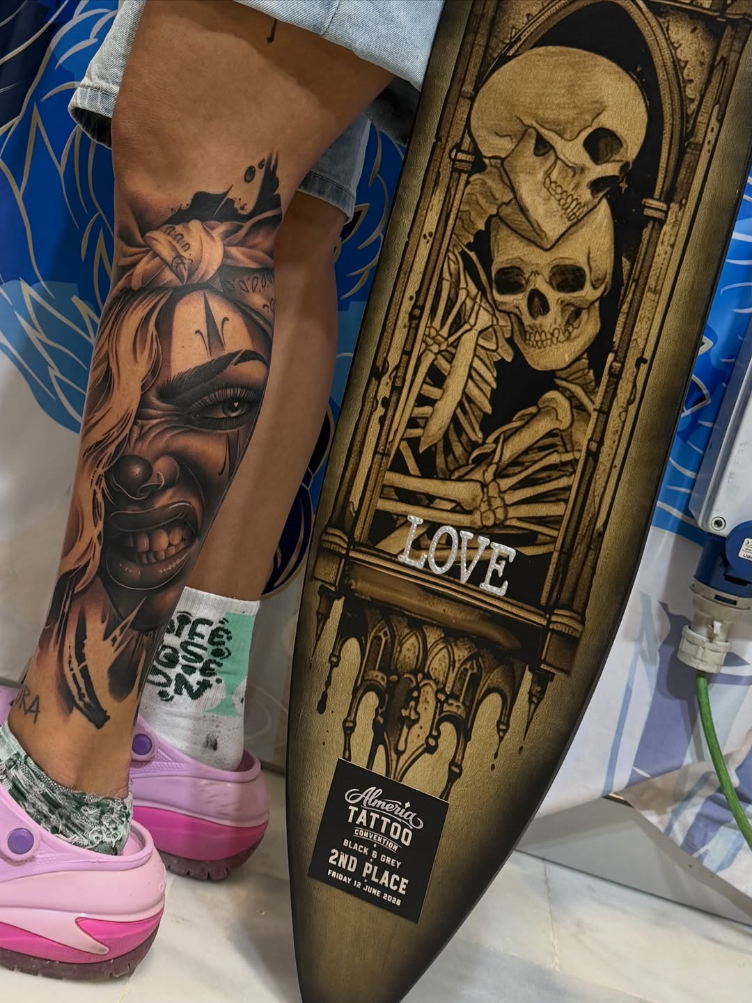 Black and grey portrait tattoo on leg featuring a woman's face with skull imagery and decorative elements.