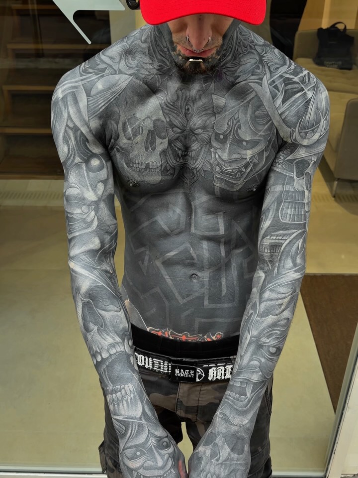 Full chest and sleeve tattoo featuring skulls and ornate designs in black and grey with smooth shading on a shirtless man.