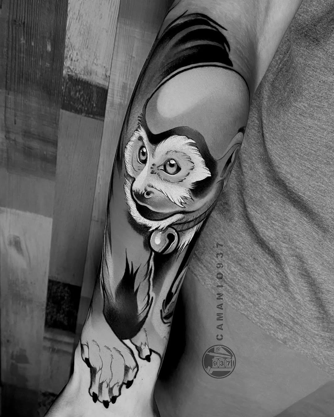 Black and grey anime lemur character tattoo on inner arm with expressive eyes and detailed fur shading.