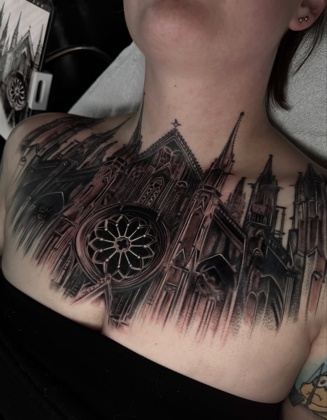 Detailed black and grey cathedral tattoo on chest featuring Gothic architecture with rose window and spires.