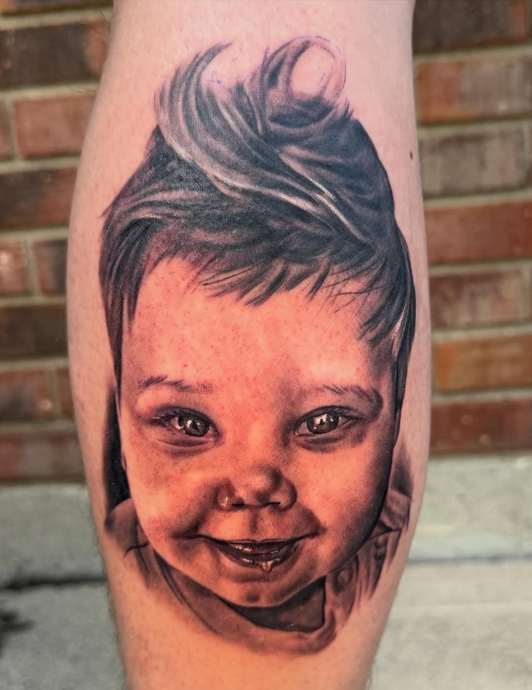 Portrait tattoo of a smiling child with styled hair on the calf in black and grey with soft shading.