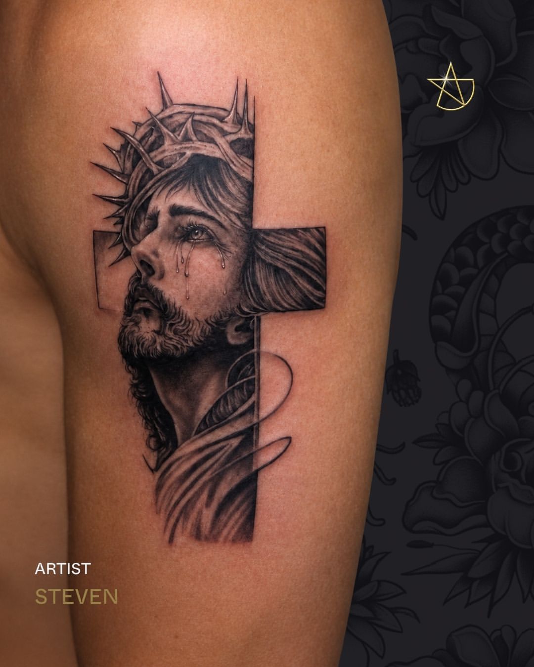 Jesus figure with crown of thorns and tears, integrated with a cross, rendered in black and grey on upper arm with smooth shading.
