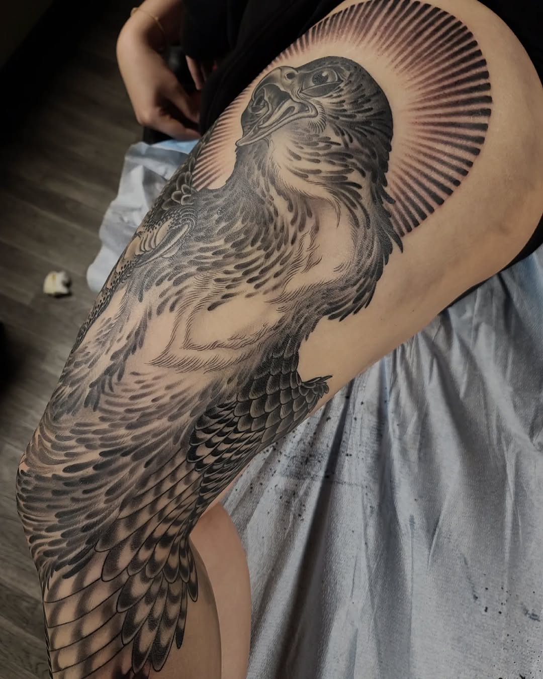 Detailed black and grey eagle tattoo with radiating lines on upper arm, showing intricate feather work and shading.
