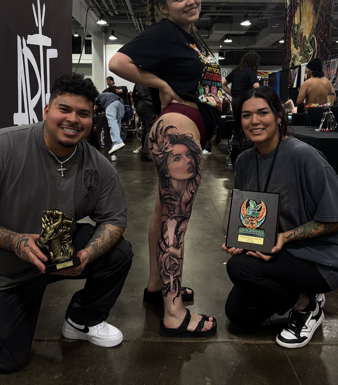 Large black and grey portrait tattoo on thigh featuring a woman's face with floral elements and decorative details.