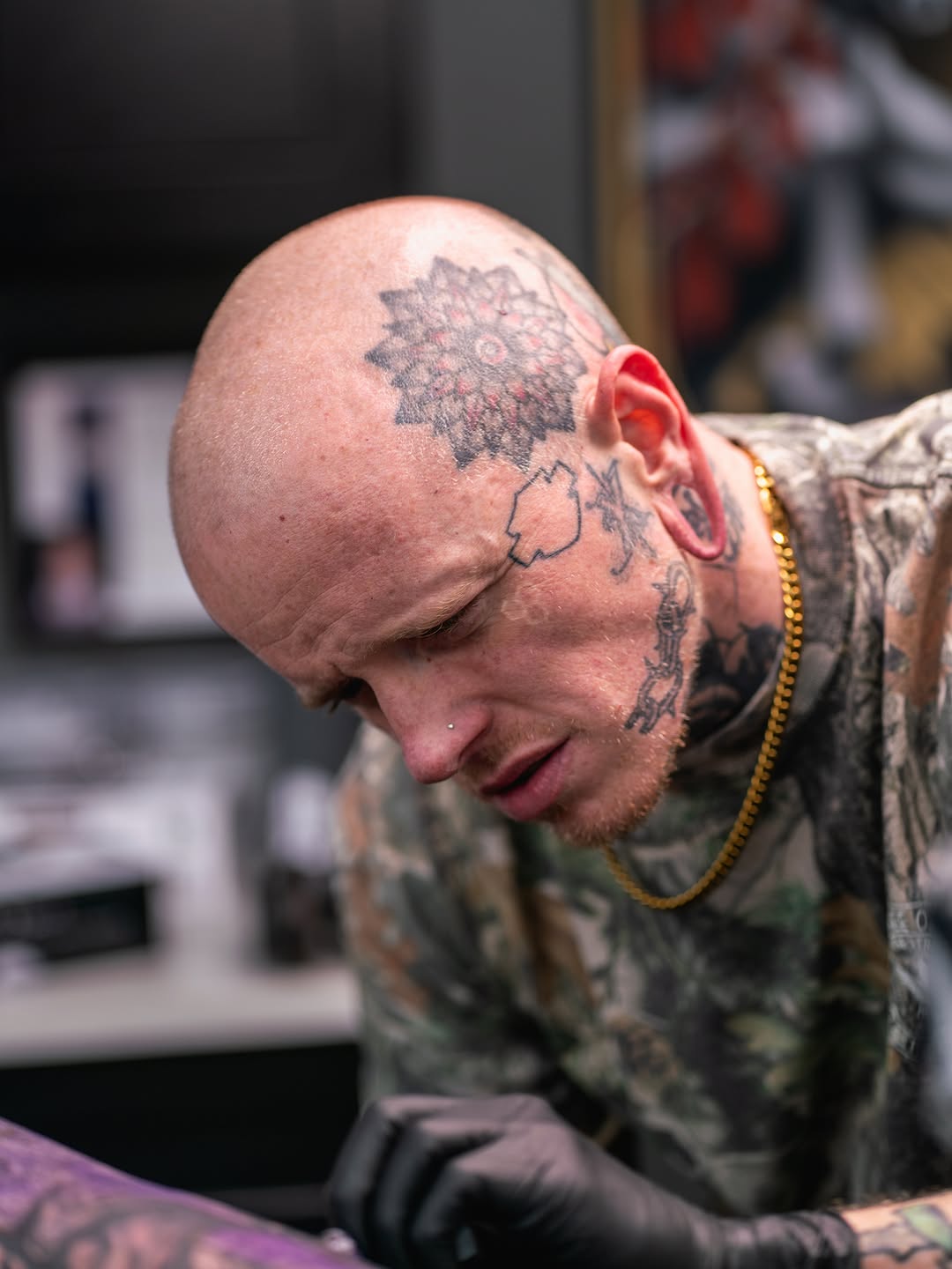 Side profile of a bald man's head and neck featuring a detailed black and grey floral tattoo with soft shading gradients.