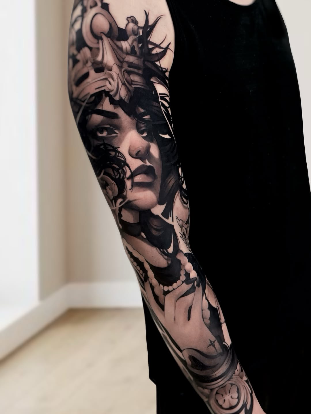 Black and grey portrait sleeve tattoo featuring a woman's face with ornate headpiece and decorative elements on the forearm.