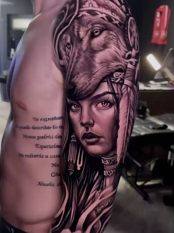 Large sleeve tattoo featuring a woman's face with an ornate lion head above, rendered in black and grey with smooth shading and Spanish text on the arm.