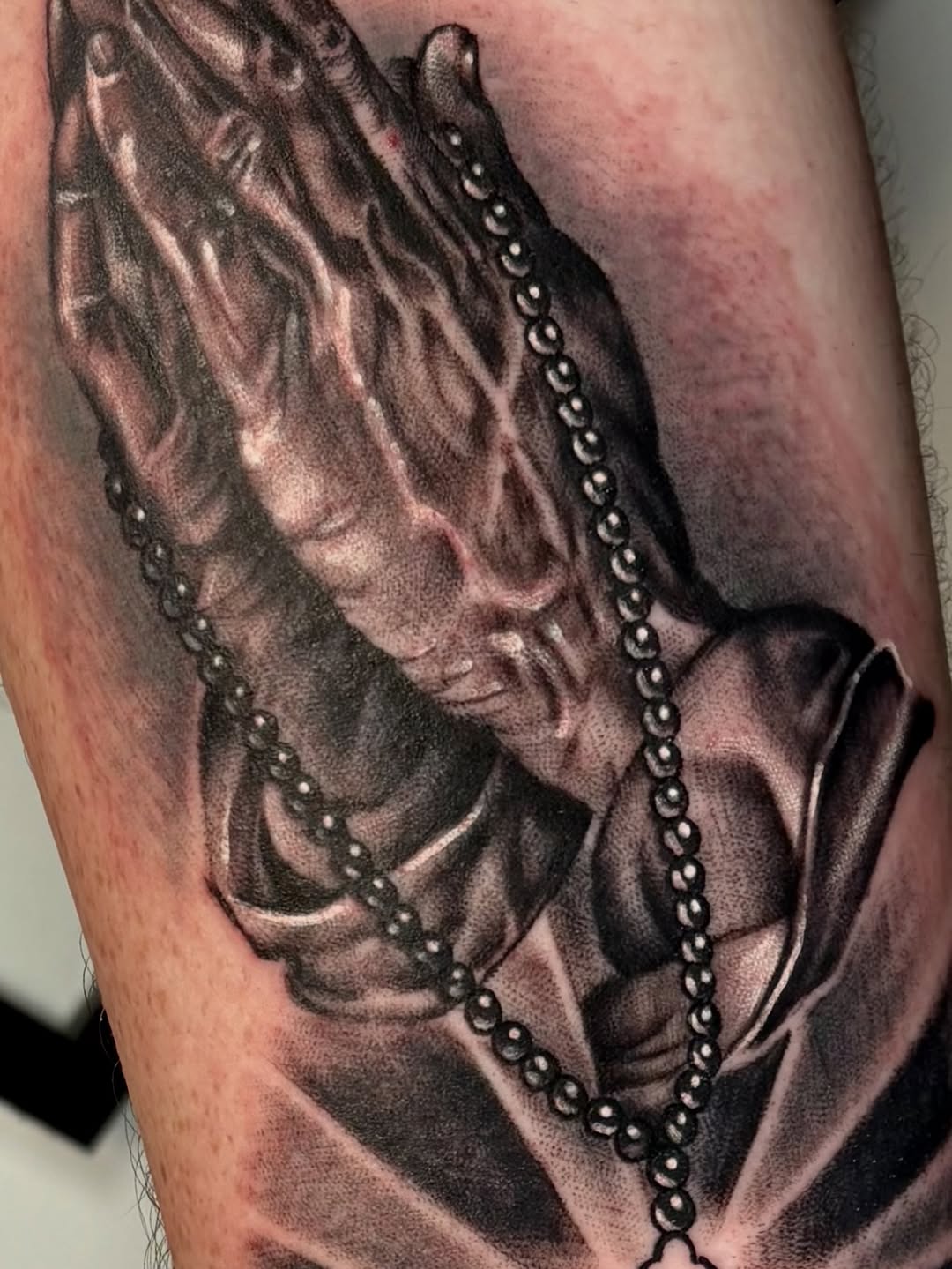 Black and grey realistic portrait of a woman wearing draped fabric and beaded chains on the upper arm.