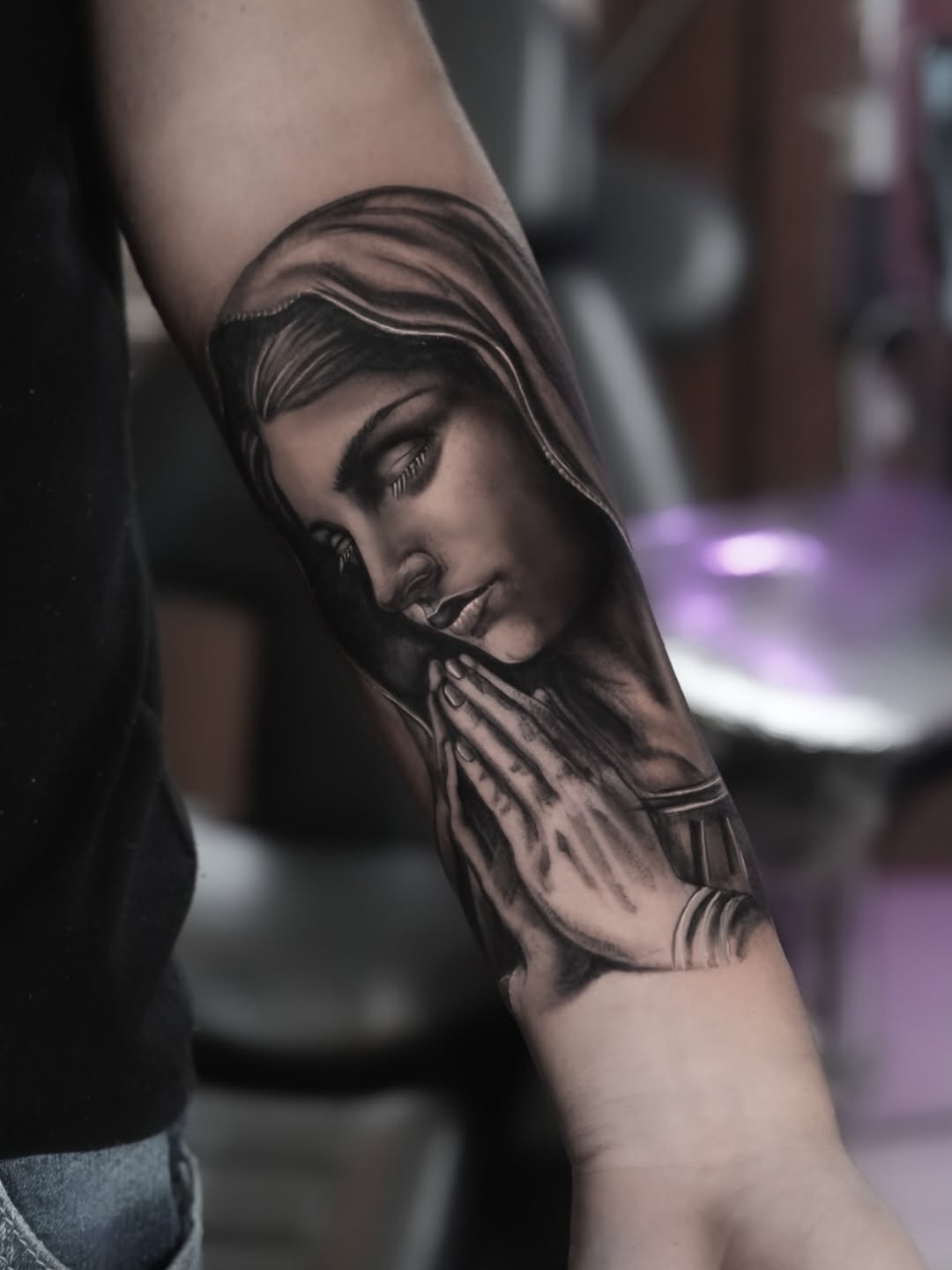 Black and grey portrait tattoo of a woman's face with long hair and closed eyes on upper arm, rendered with smooth shading gradients.