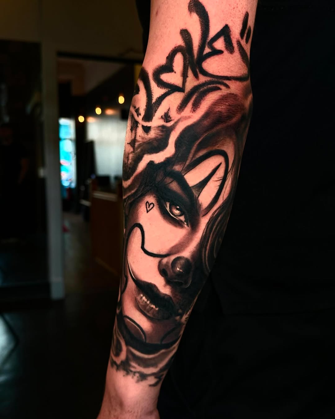 Black and grey demon face tattoo on the leg with horns, detailed shading, and a small heart marking on the cheek.