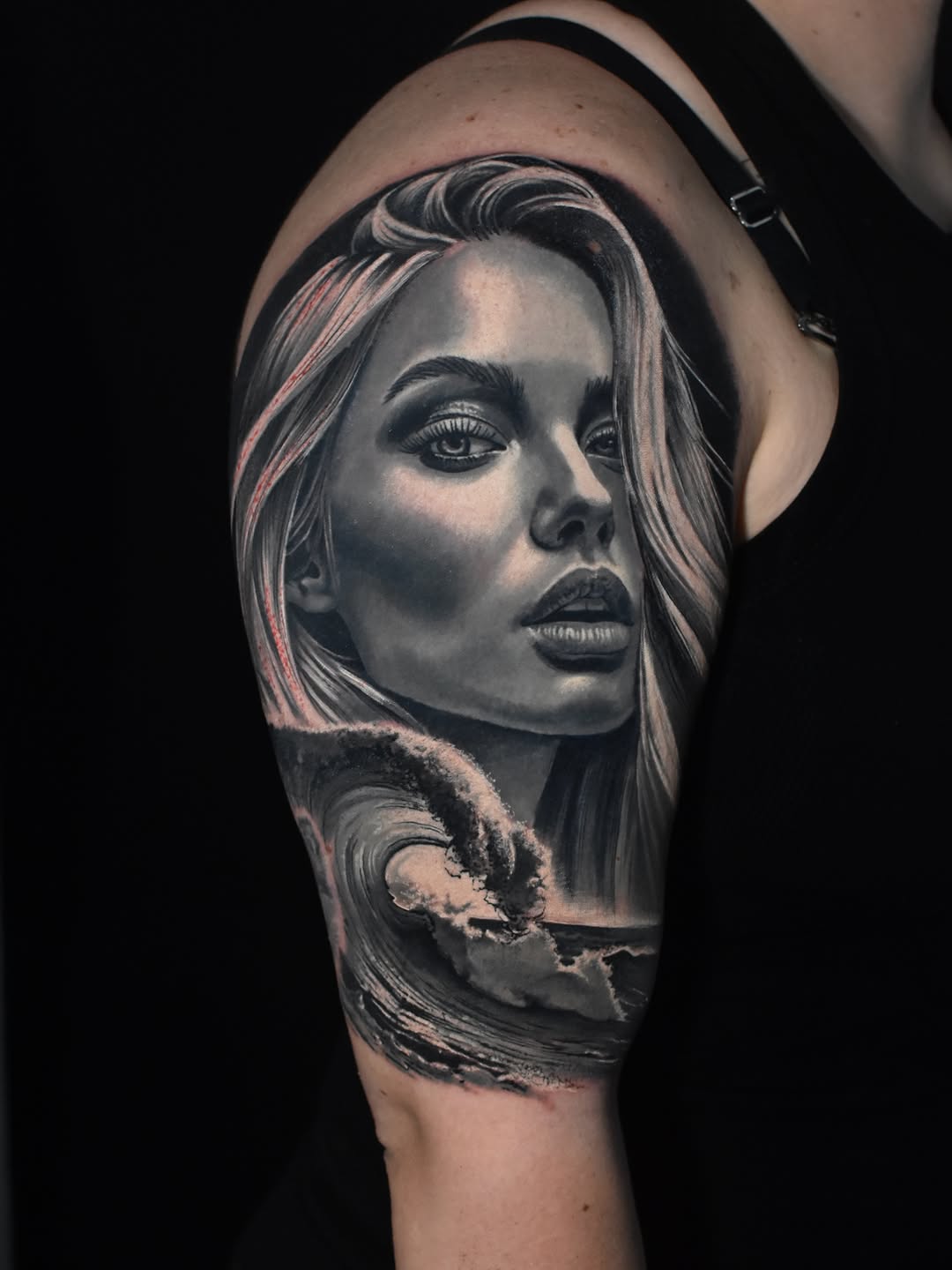 Black and grey portrait tattoo of a woman's face with long hair and subtle shading on the upper arm.