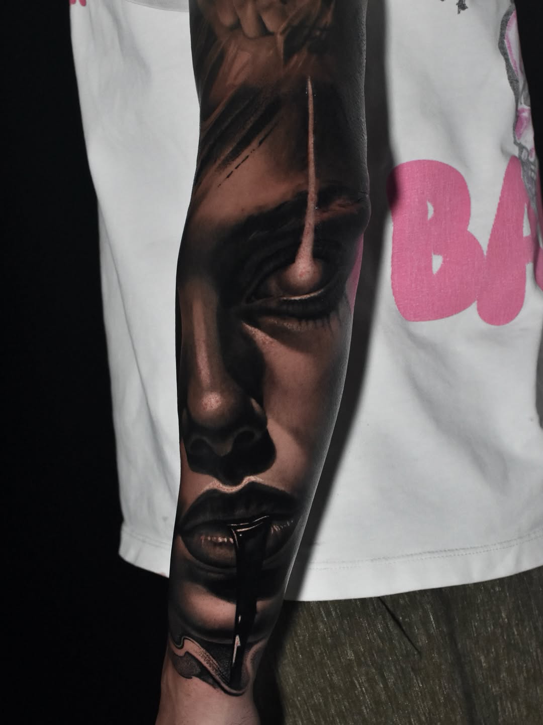 Black and grey realistic tattoo of a woman's face with closed eye and lips on forearm sleeve, dark shading.