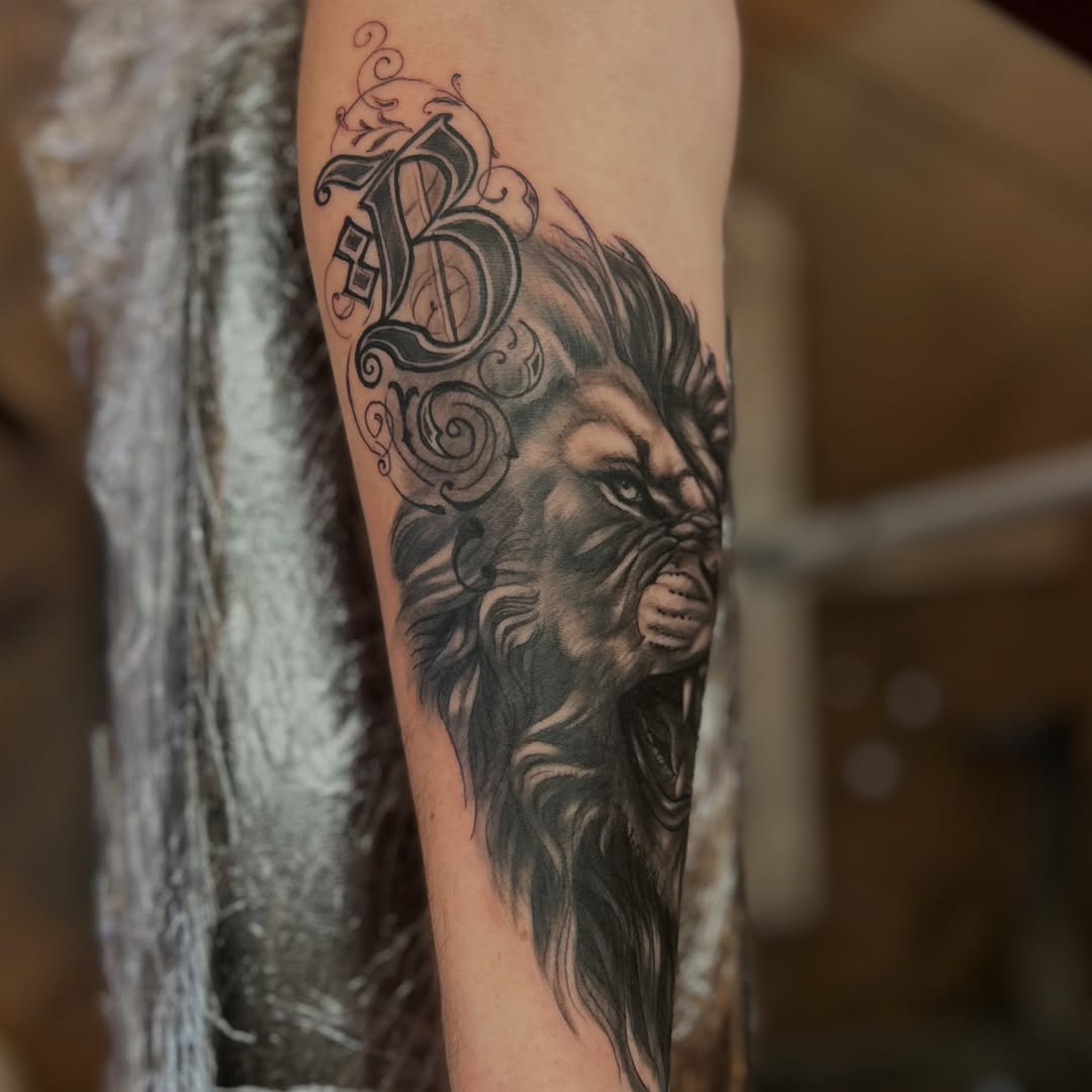 Demon or beast face with ornate decorative scrollwork crown on upper arm, rendered in black and grey with soft shading.