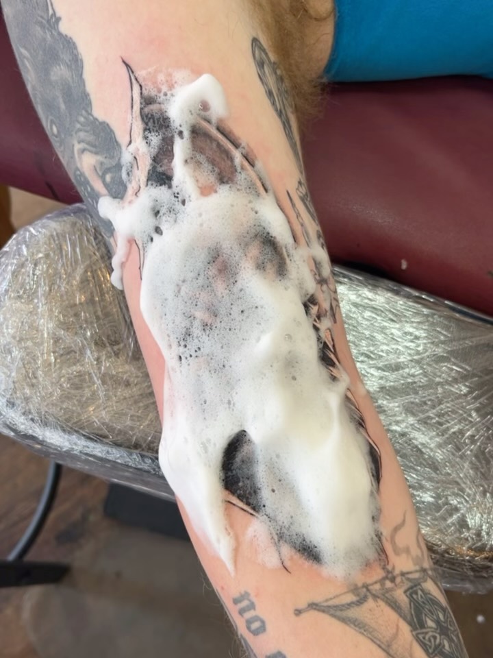 Black and grey horse head tattoo on forearm with realistic shading and soft gradients, surrounded by other tattoos.