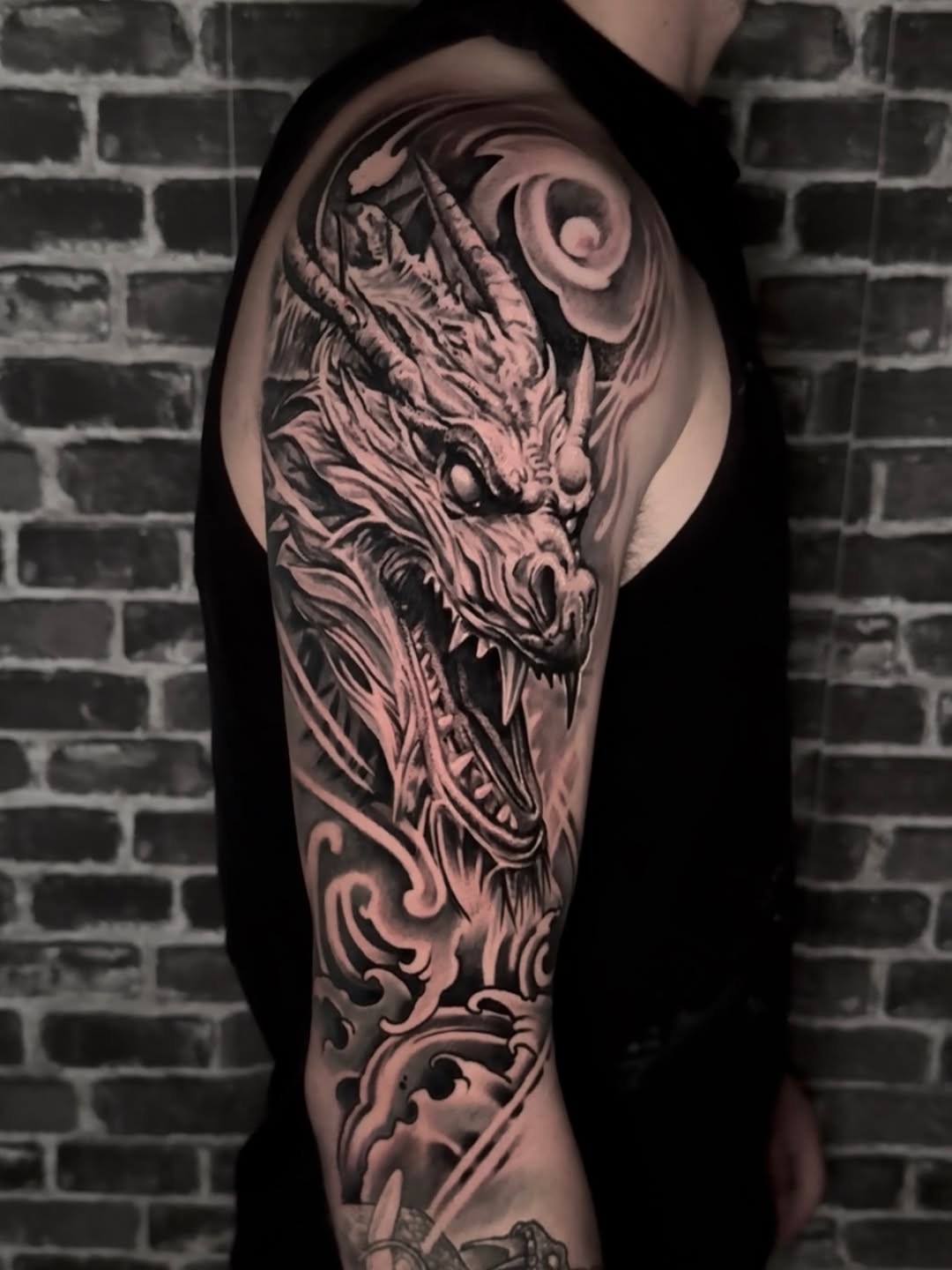 Detailed dragon head tattoo on upper arm with ornate scrollwork, rendered in black and grey with smooth shading gradients.