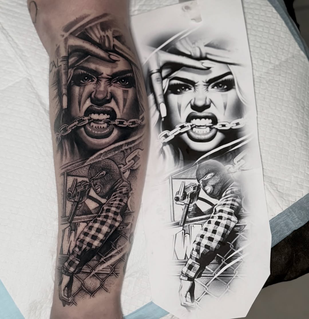 Angry face with chain through mouth and armed figure below in black and grey on forearm, with design sketch beside it.