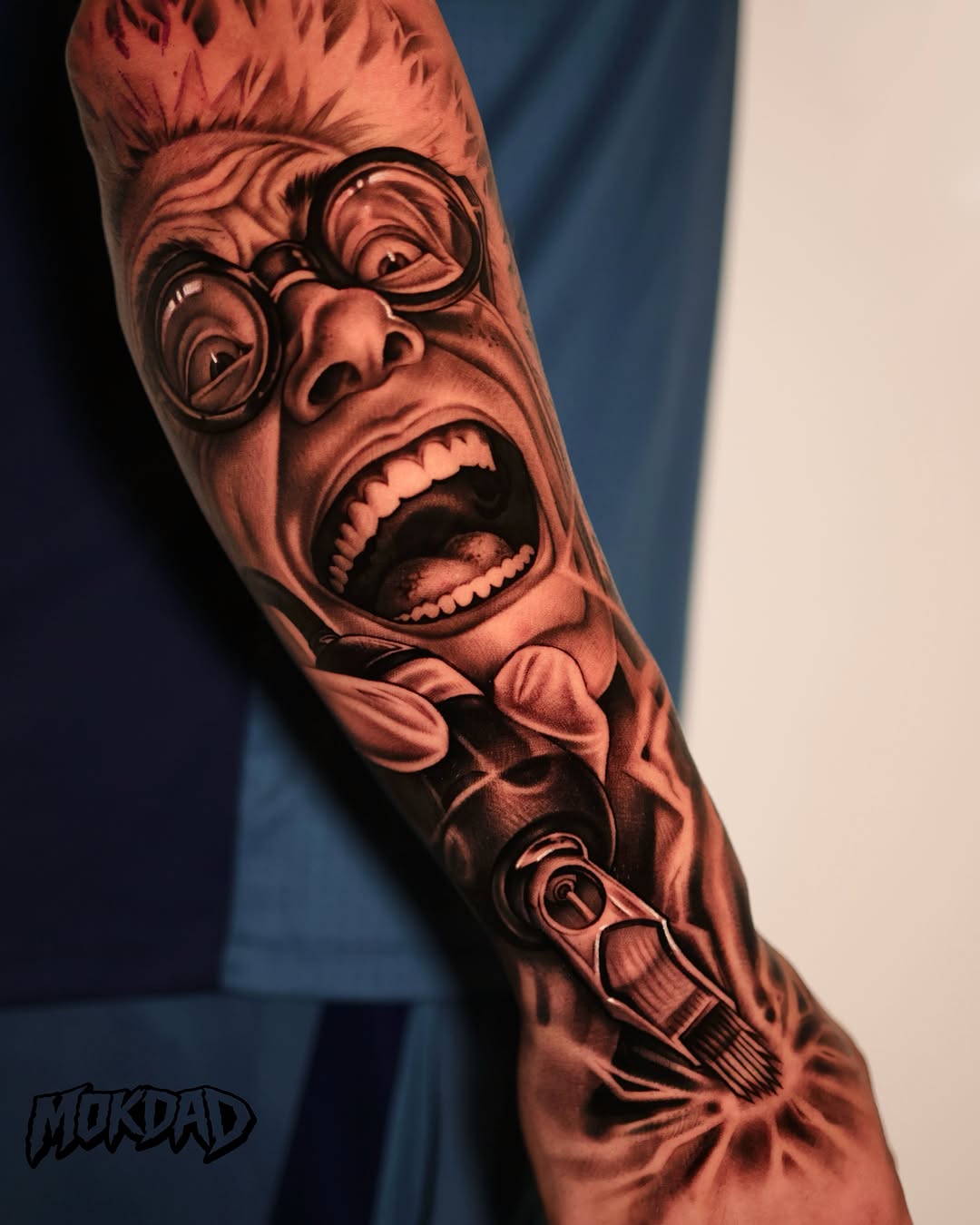 Black and grey realistic portrait tattoo of an expressive face with glasses and open mouth on upper arm.
