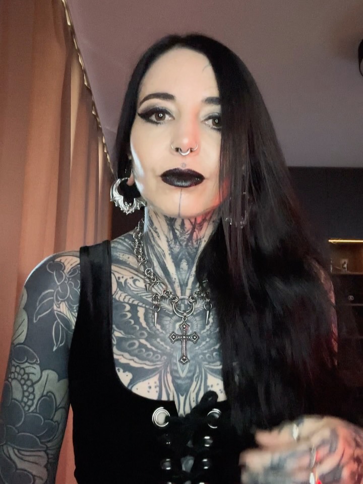 Chest and neck tattoo featuring ornate floral patterns in black and grey shading on a person with long dark hair.
