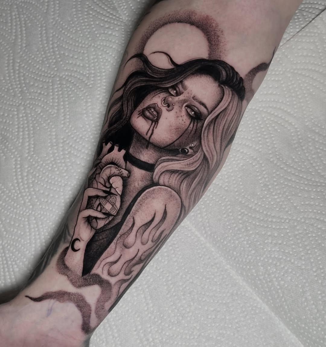 Black and grey portrait tattoo of a woman with long wavy hair, facial piercings, and hand gesture on forearm.