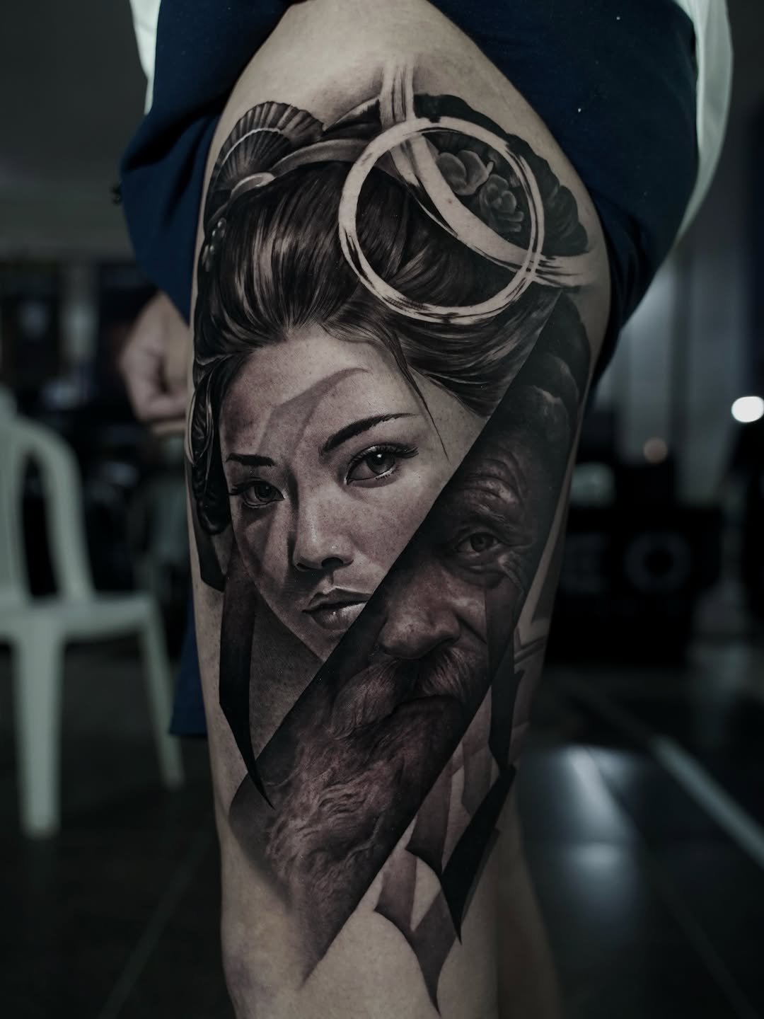 Black and grey portrait tattoo on upper arm featuring a woman with goggles and a bearded man's face in profile, rendered with smooth shading.