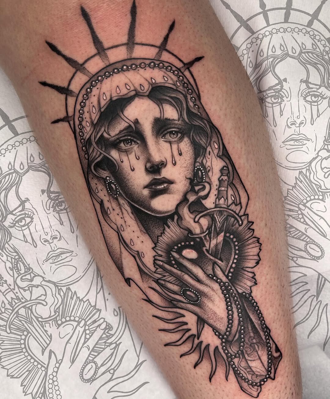 Black and grey portrait tattoo of a woman with a halo and tears on the upper arm, featuring decorative ornamental elements and jewelry details.