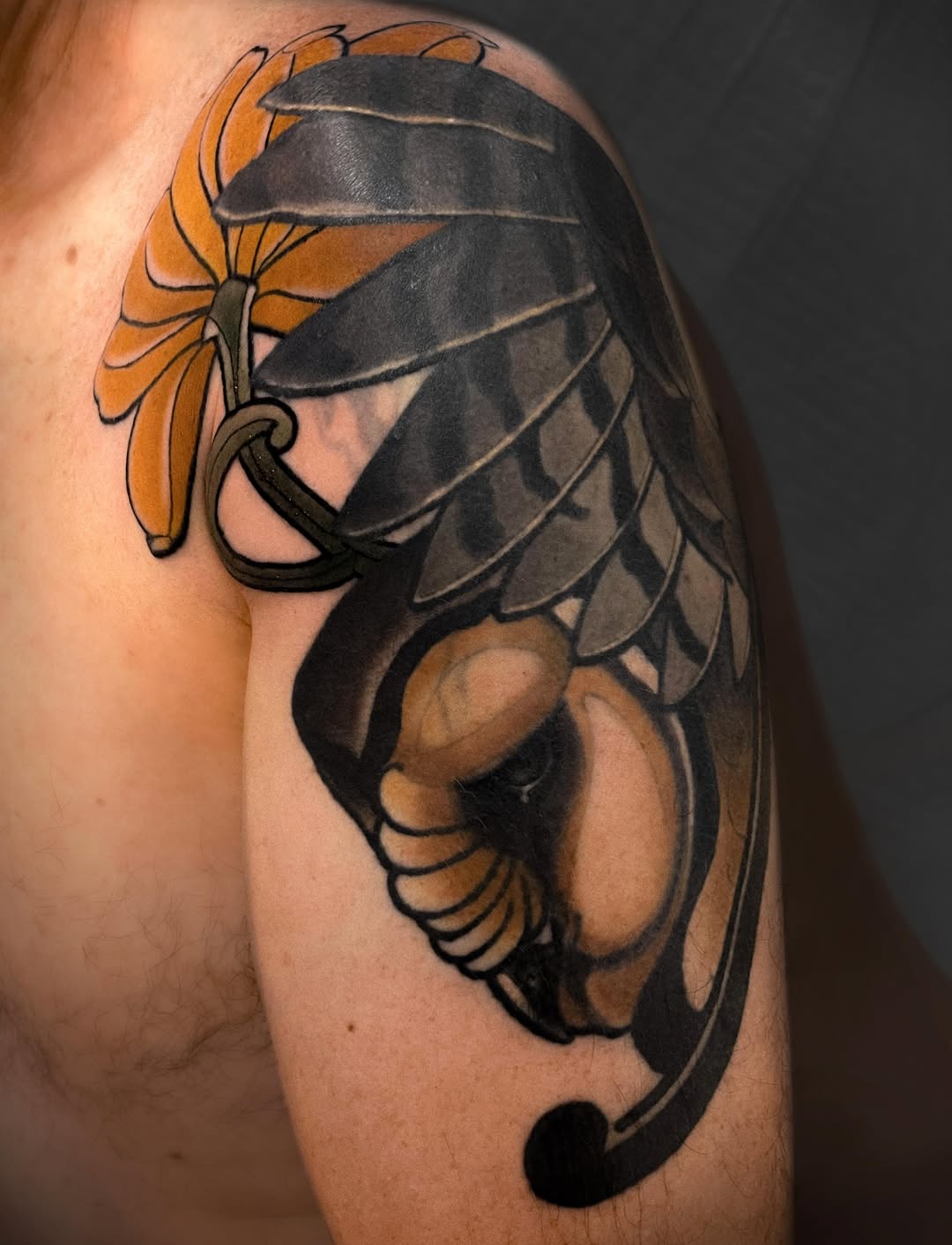 A scorpion with spread wings and a yellow flower held in its claws, rendered in black and grey shading on the upper arm.