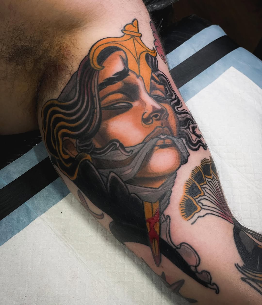 Bearded male bust with ornate crown and decorative elements in black and grey on upper arm.