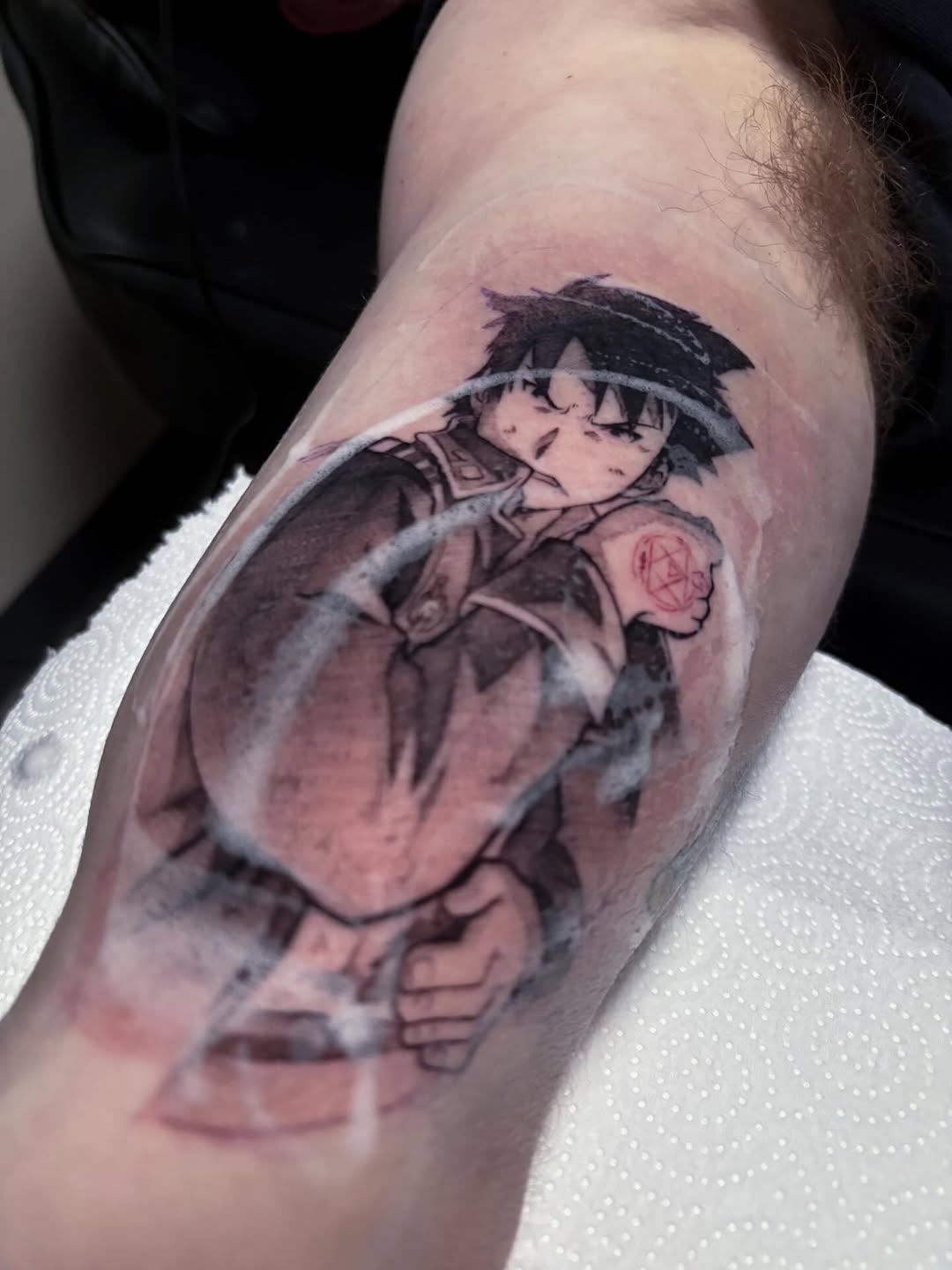 Anime character with black hair and closed eyes wearing brown clothing with a red symbol on arm, tattooed on upper arm in black and grey shading.
