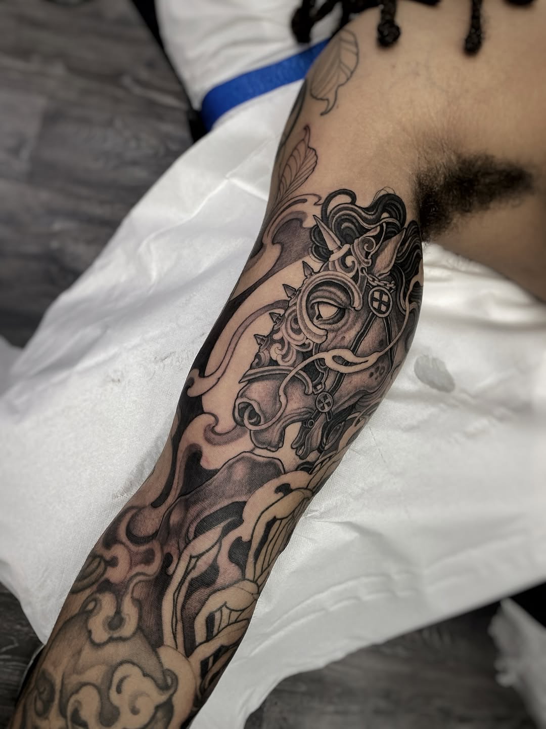 Ornate baroque-inspired sleeve tattoo with scrollwork, decorative elements, and an eye motif in black and grey shading on the arm.