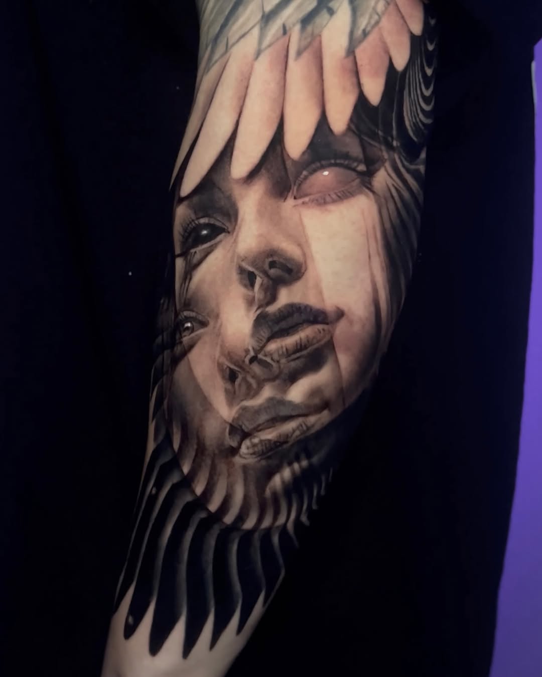 Black and grey portrait tattoo on arm featuring a woman's face with bangs and feathered wing design, rendered in soft shading.