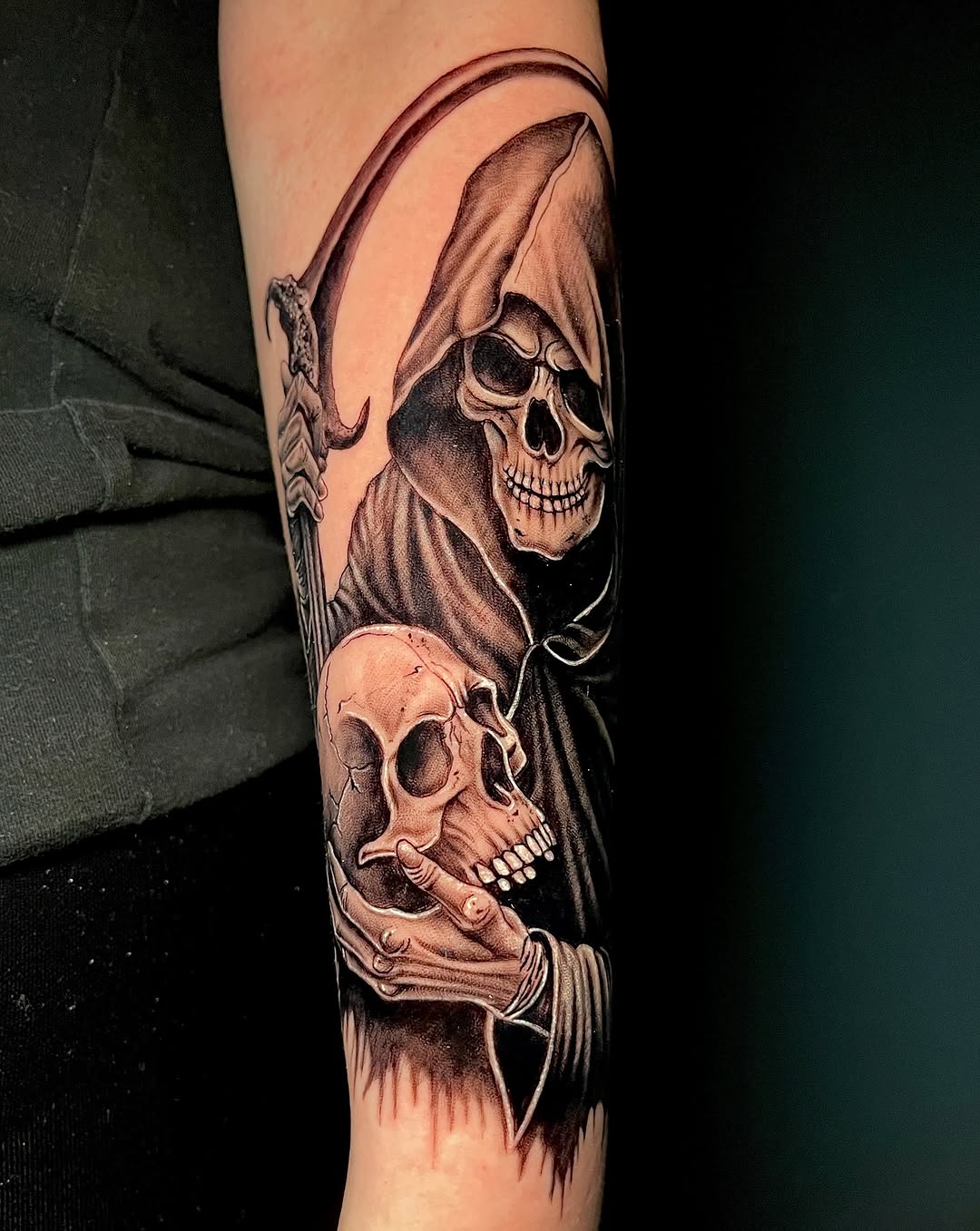 Grim reaper holding skulls in hooded robes on forearm, rendered in black and grey with detailed shading.