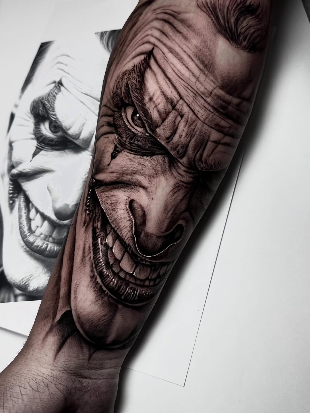 Black and grey realistic portrait tattoo of a face with skull imagery on the upper arm showing detailed shading and depth.