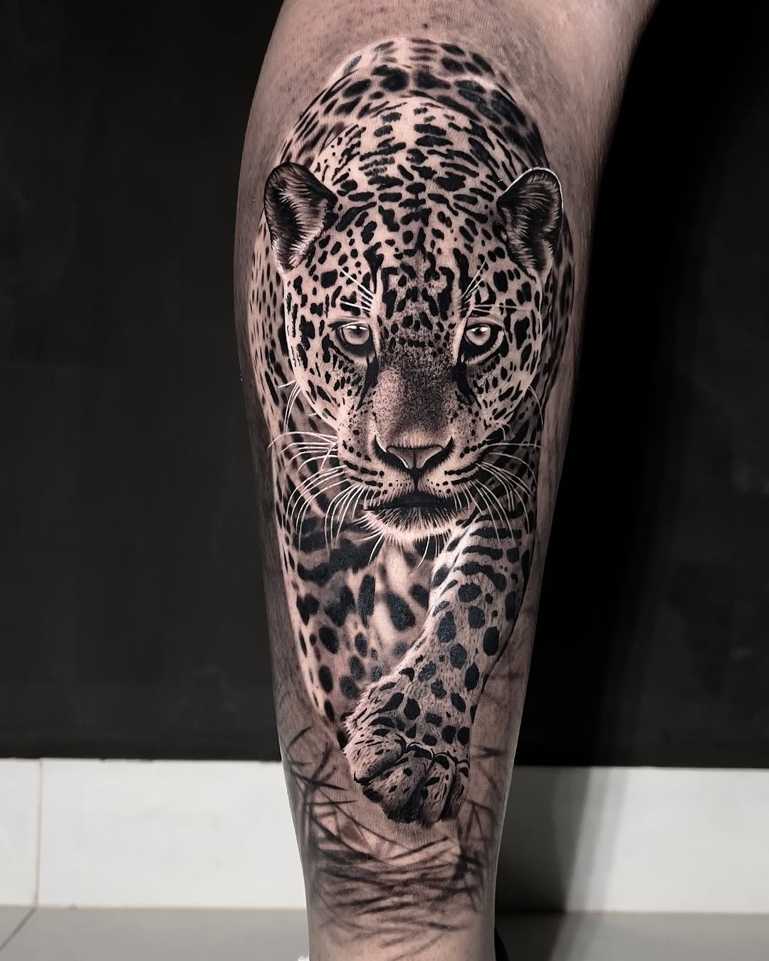 Detailed black and grey leopard head with piercing eyes and spotted pattern on forearm, with paw visible below.