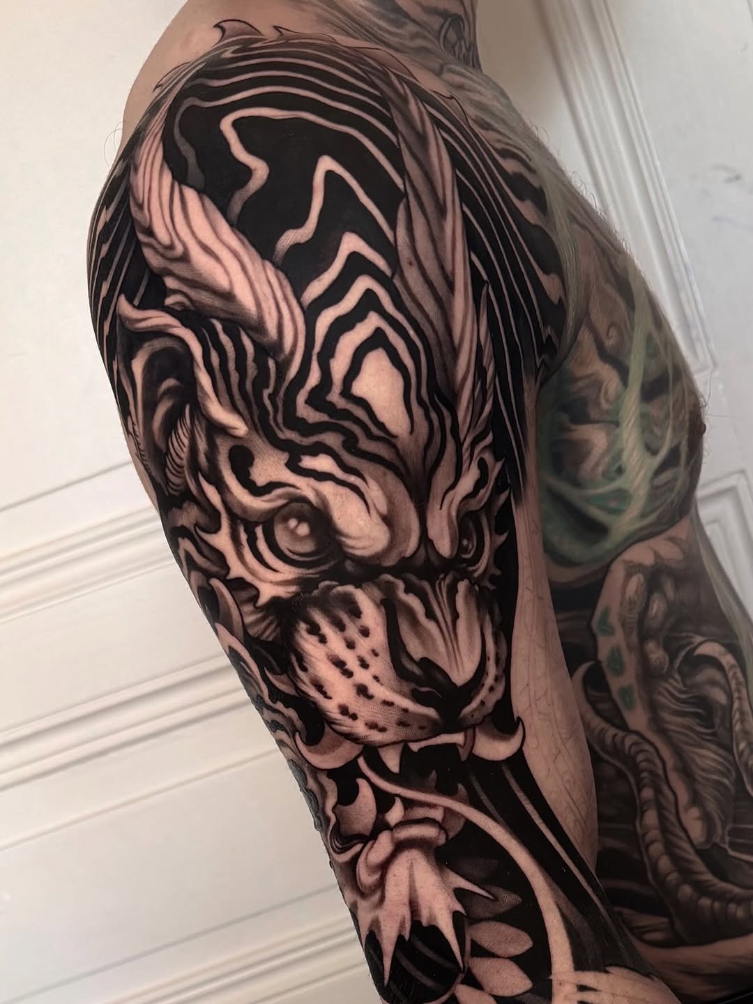 Detailed black and grey tiger head tattoo on upper arm with flowing mane and fierce expression, surrounded by decorative flourishes.
