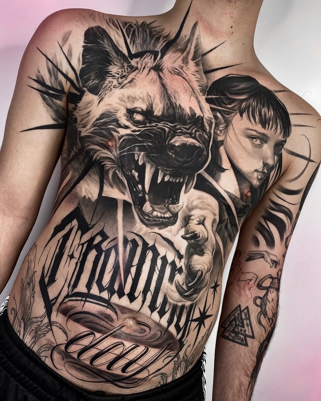 Aggressive roaring lion head with human faces and script text on chest and torso in black and grey shading.