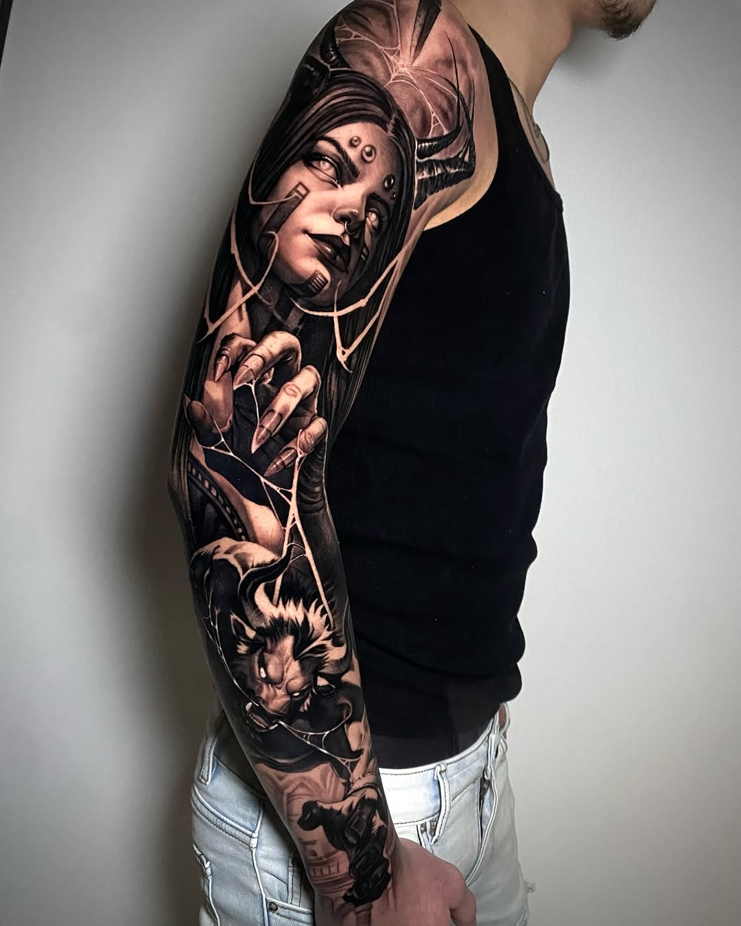 Full arm sleeve tattoo featuring a portrait of a woman's face with ornate details, a lion, and flowing linework in black and grey shades.