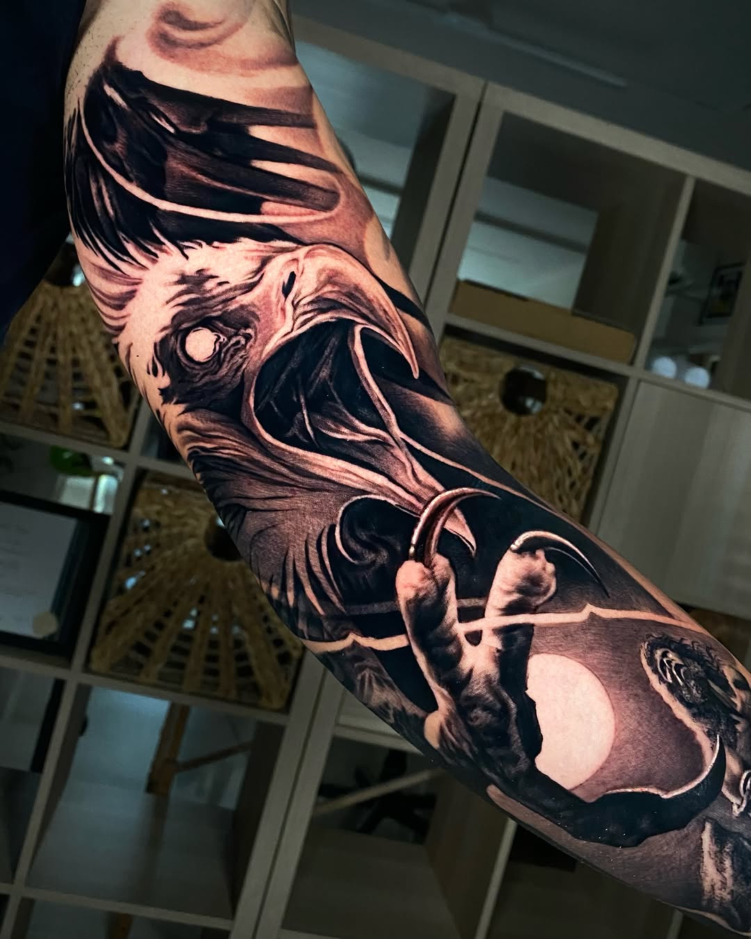 Black and grey eagle head tattoo with flowing feathers and a crescent moon on the forearm, featuring smooth realistic shading.