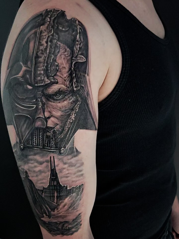 Black and grey portrait tattoo of Darth Vader with TIE fighter below on upper arm, featuring detailed realism and shading.