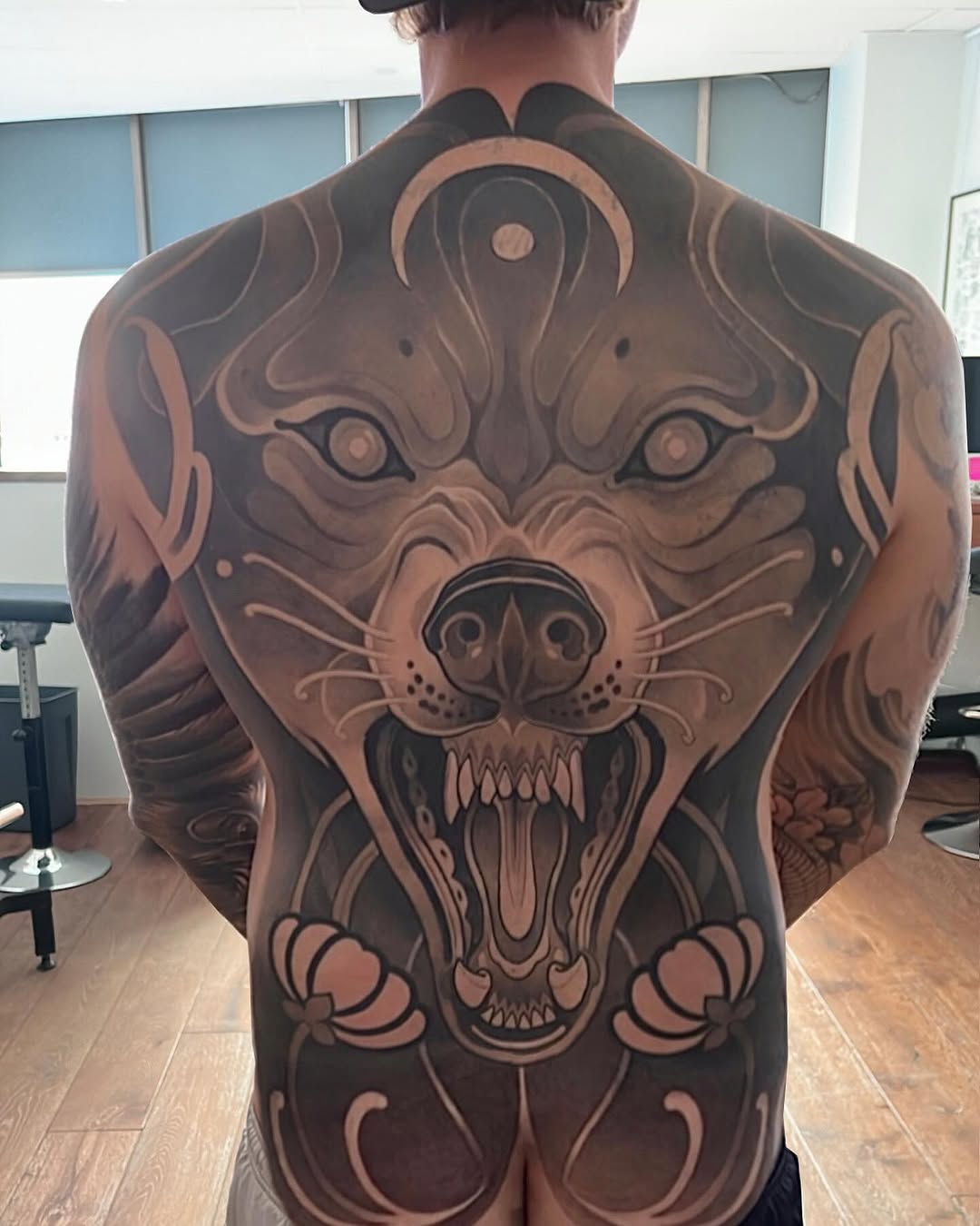 Large back tattoo of a fierce roaring bear head with detailed shading in black and grey tones, spanning shoulders to lower back.