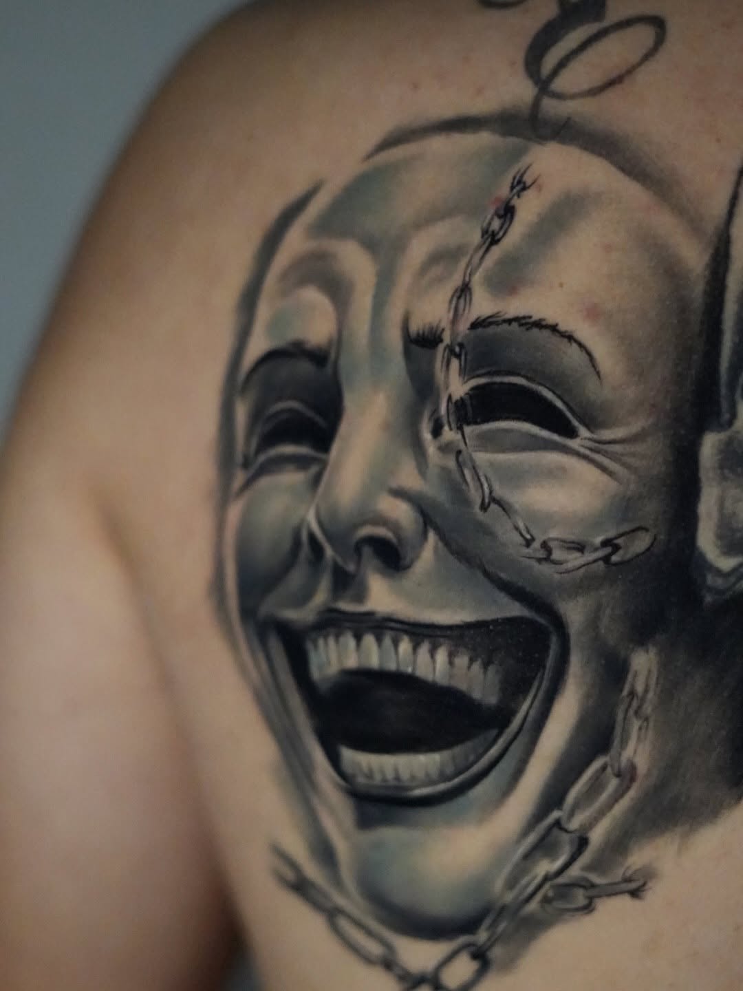 Two screaming demon faces with stitched mouths and chain details, rendered in black and grey shading on shoulder.