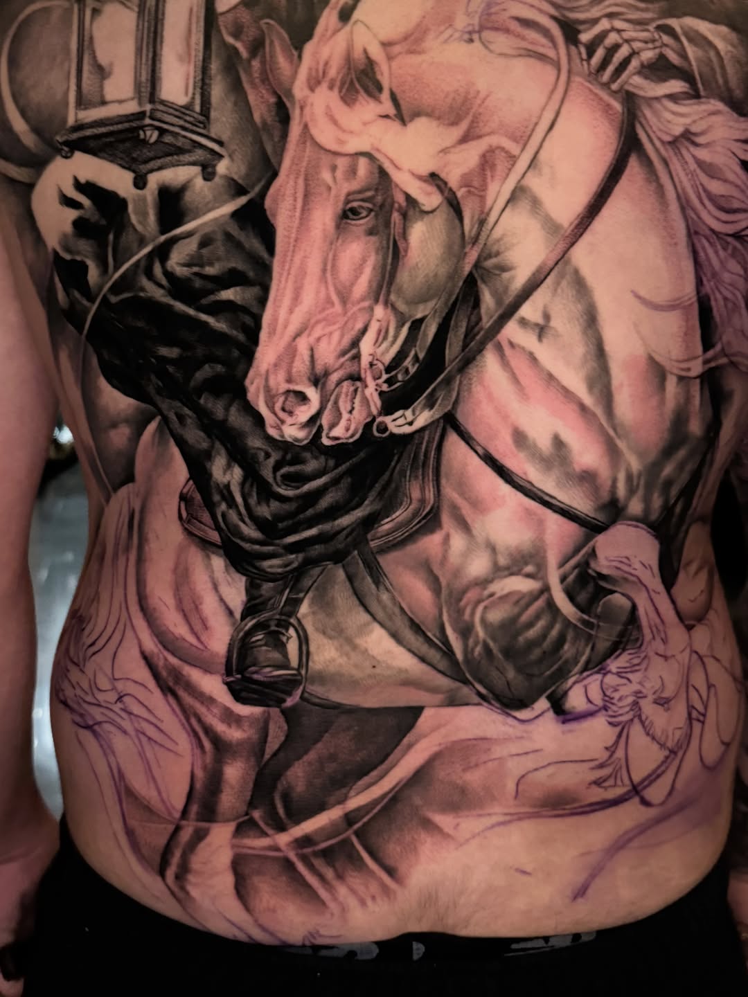 Large black and grey back tattoo of a horse's head with bridle and reins, plus lantern and additional linework in progress.