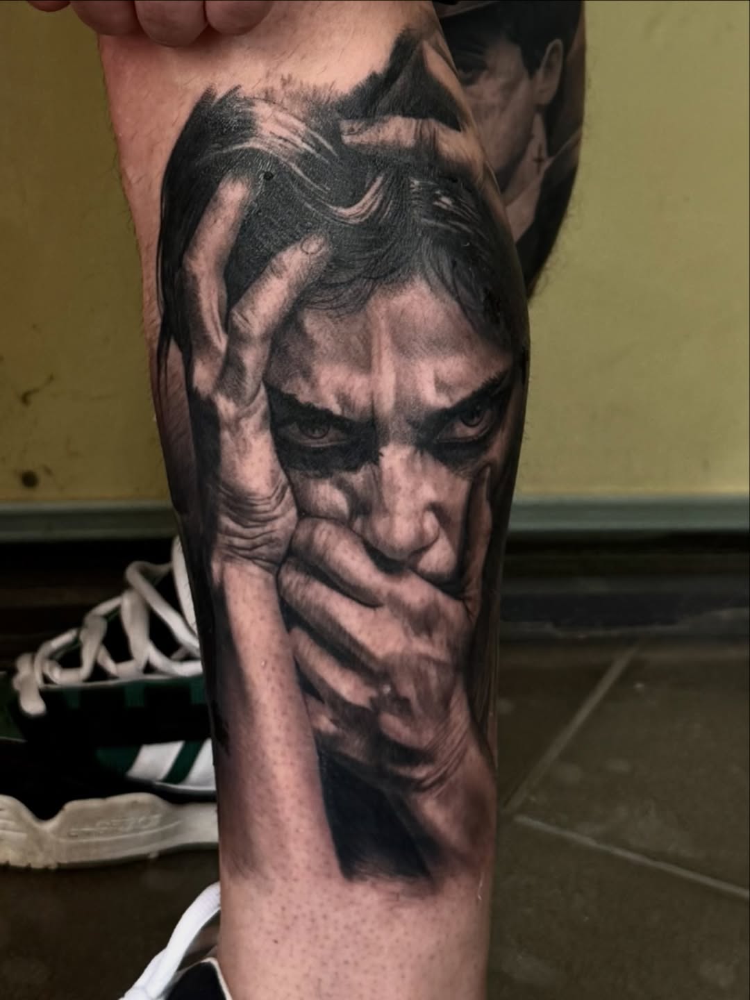 Black and grey portrait tattoo of a man's face with dramatic shading on the upper arm.