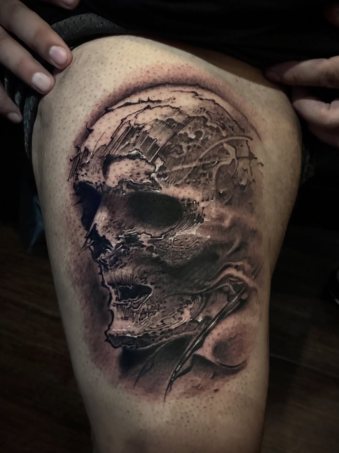 Detailed black and grey skull tattoo on thigh with realistic shading and anatomical detail, displayed on skin.