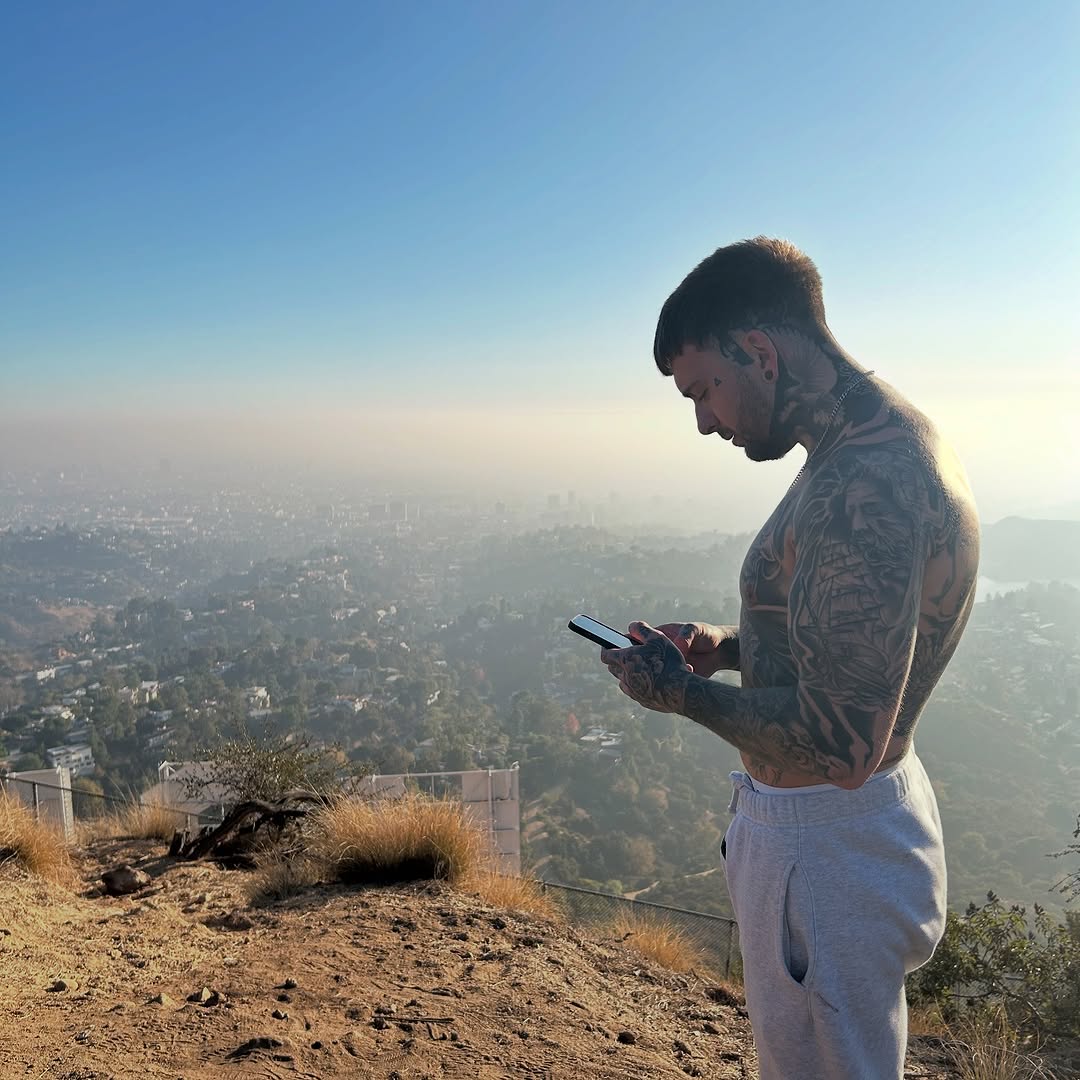 Large black and grey back tattoo featuring detailed portrait and ornamental designs on shirtless man overlooking city landscape.