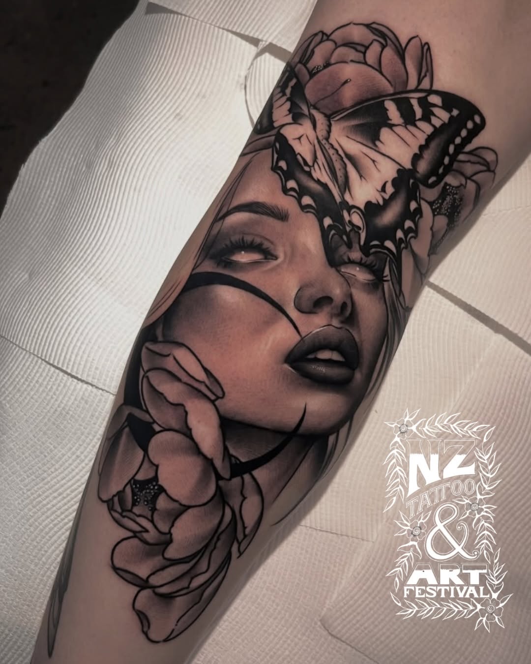 Woman's forearm tattoo featuring a contemplative female face with closed eyes, surrounded by detailed peonies and a swallowtail butterfly, rendered in black and grey.